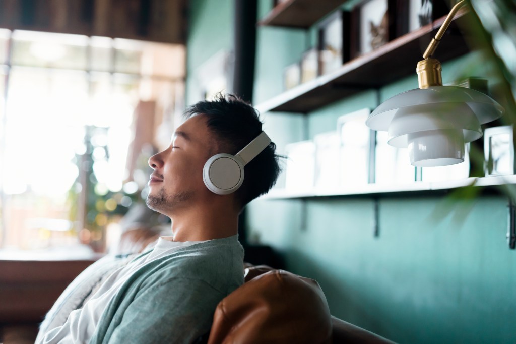 Young asian boy with eyes closed enjoying music with headphones while relaxing on sofa at home