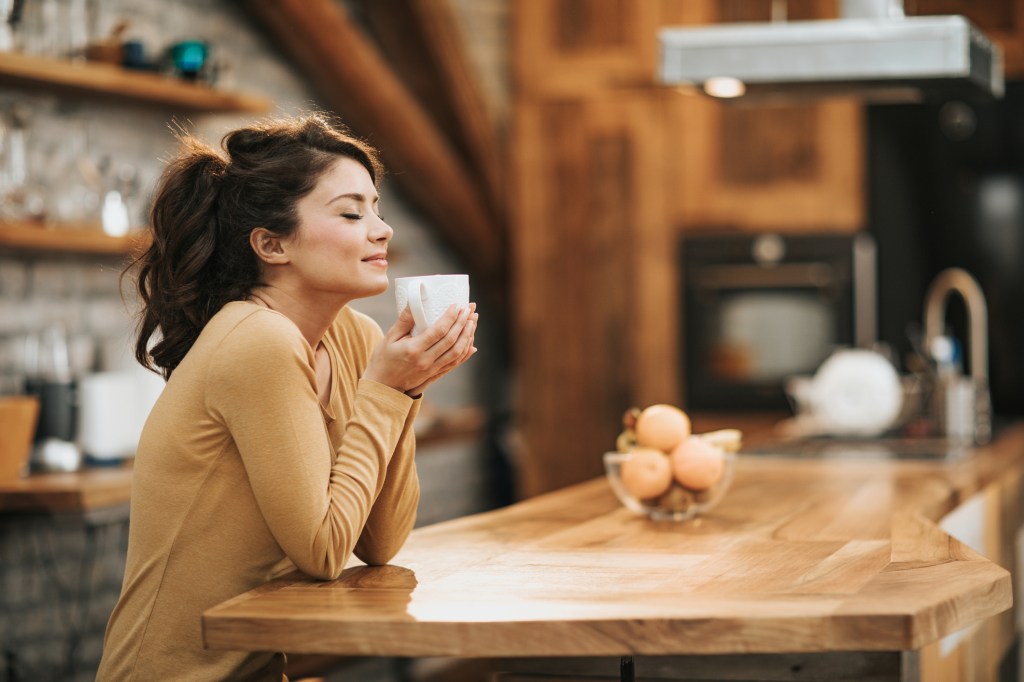 Young woman enjoying a smell of fresh coffee in the kitchen.